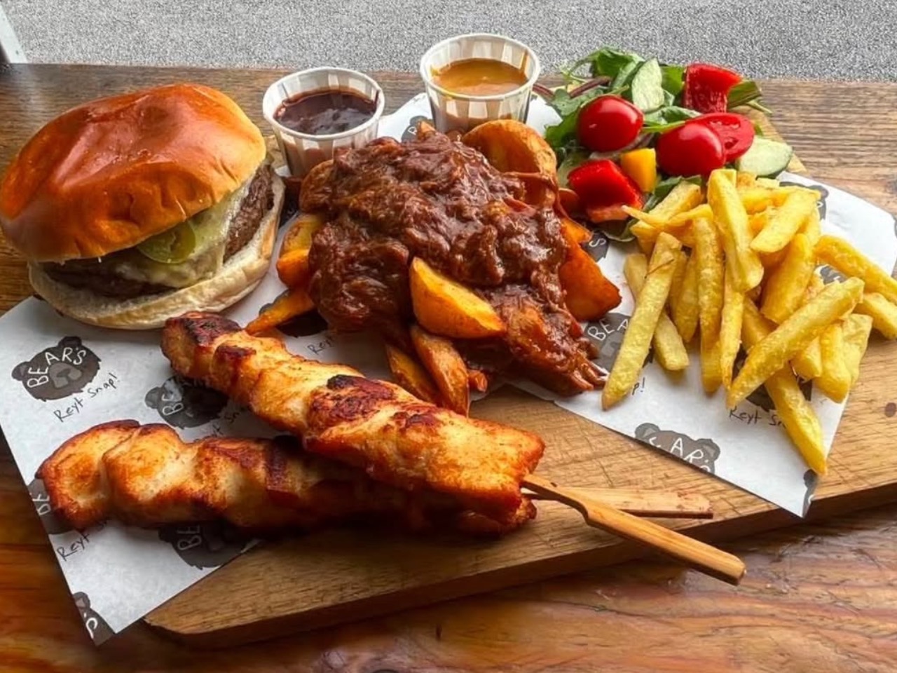 A double beef smash burger with melted cheese served alongside french fries and grilled chicken skewers for TV & film catering.