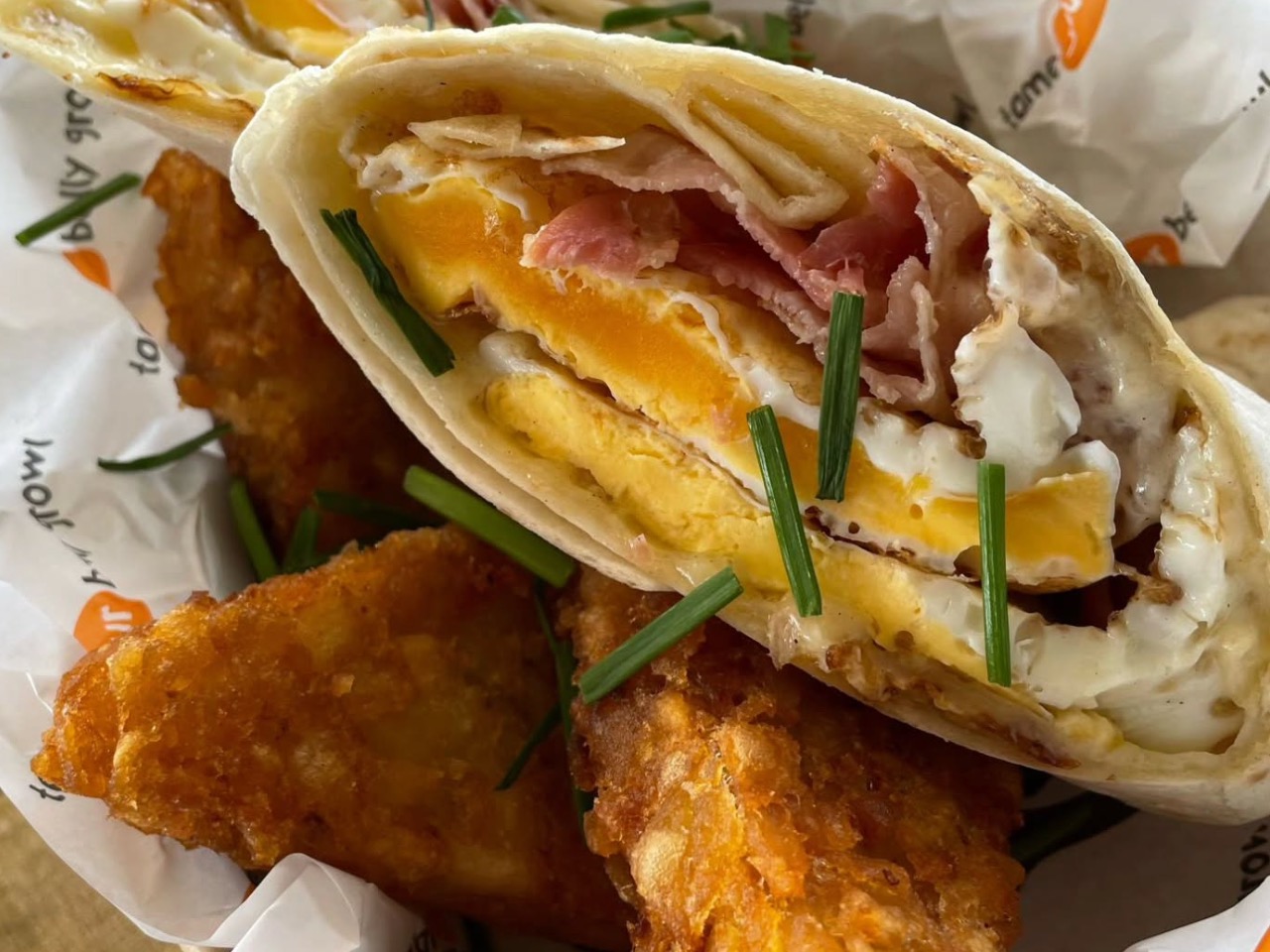 A loaded breakfast roll cut open displaying a runny fried egg, crispy bacon, and golden hash browns for early morning TV & film catering.