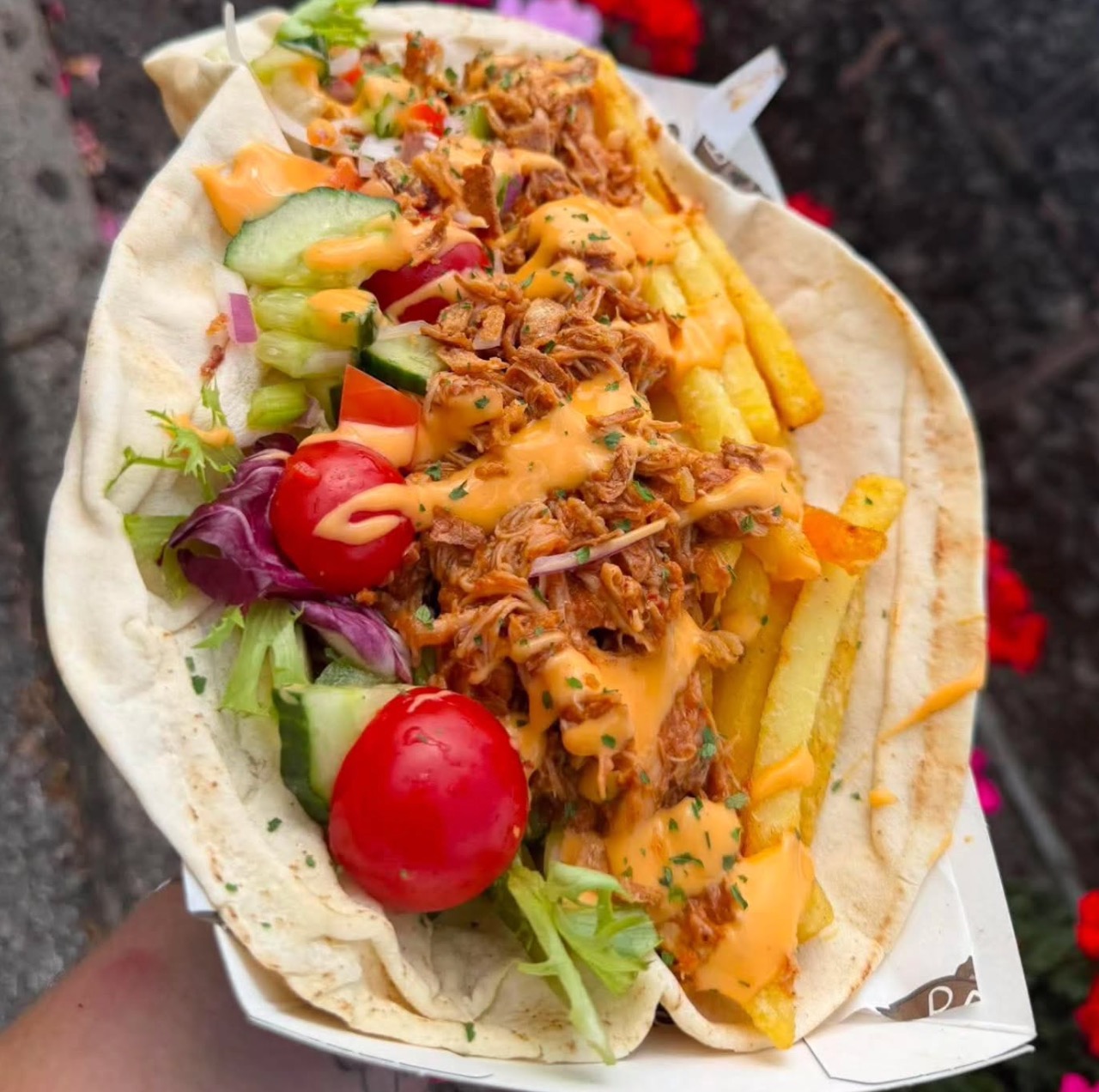 A warm open flatbread loaded with shredded marinated chicken, crisp salad greens, cherry tomatoes and garlic mayo, served for workplace canteen catering.