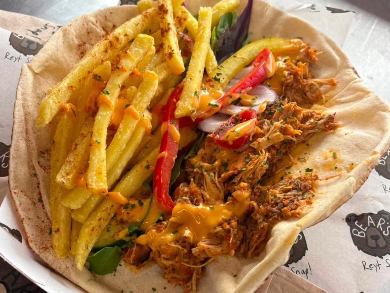 Soft warm flatbread filled with tender smoked pulled meat, french fries and tangy sauce served outdoors for workplace canteen catering.