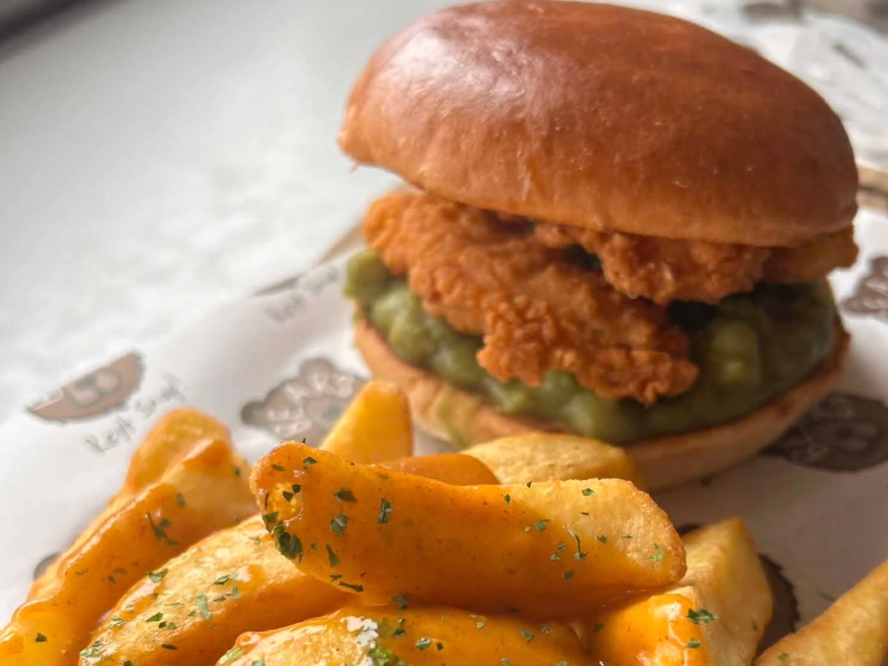 Golden panko-crusted fish fingers stacked in a soft brioche bun with mushy peas and tartare sauce for workplace canteen catering.